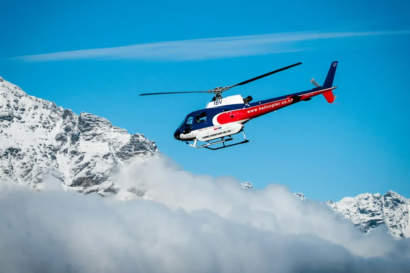 Helikopter im Flug vor verschneiten Gipfeln über einer Wolkenbank