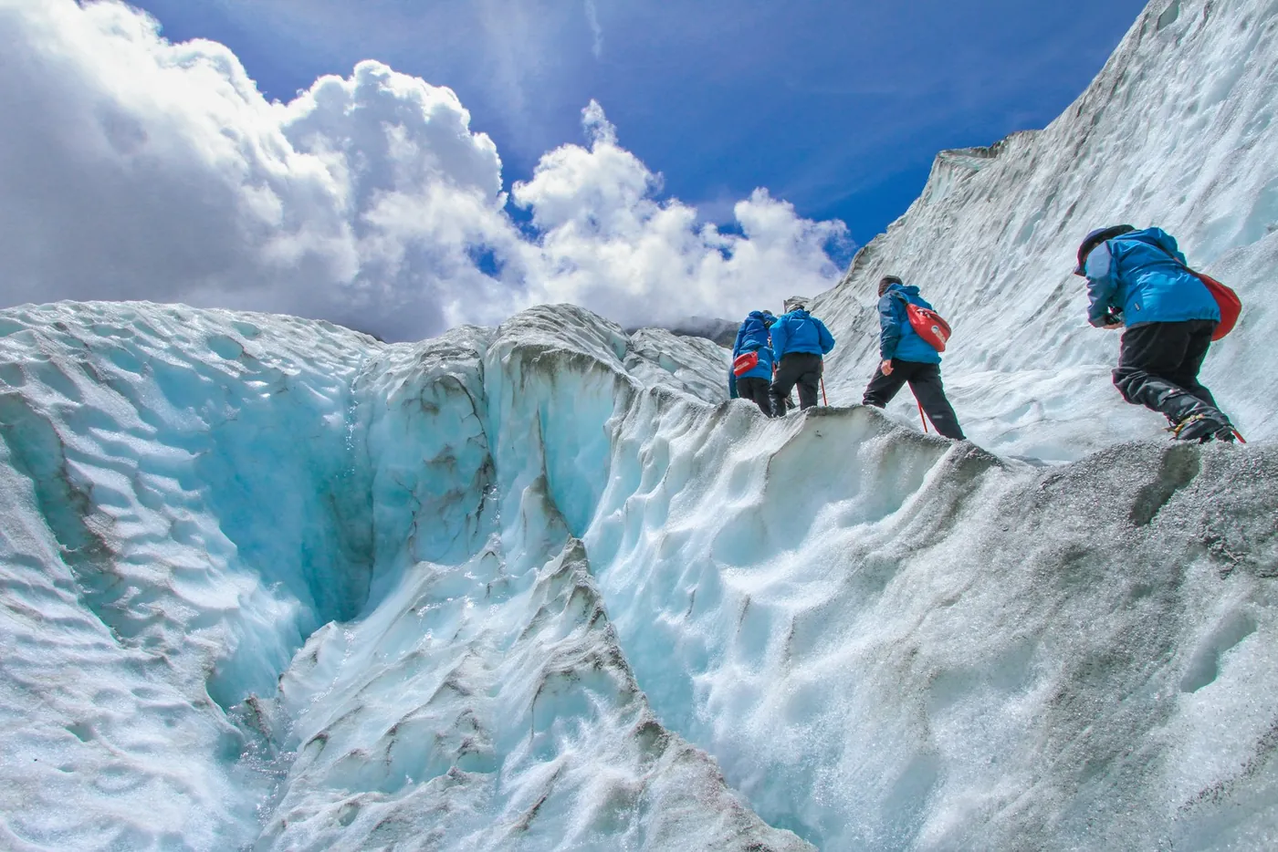 Grupo con guía caminando sobre hielo azul en el glaciar Franz Josef
