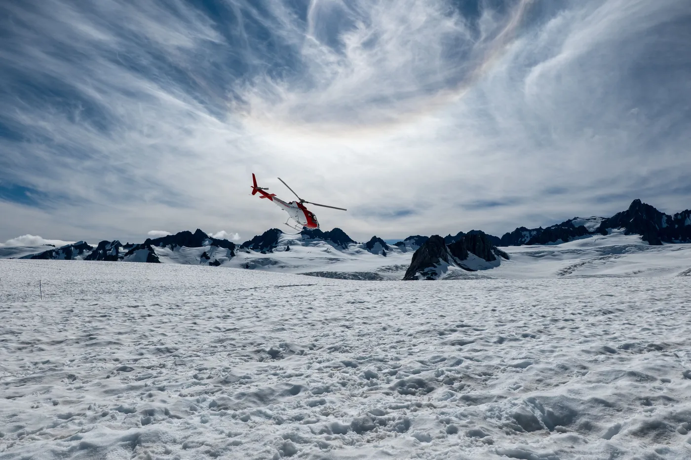Helikopter über einem weiten Gletscher-Schneefeld unter dramatischem Himmel