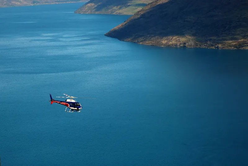 Helikopter über dem tiefblauen Wasser eines Bergsees bei Queenstown