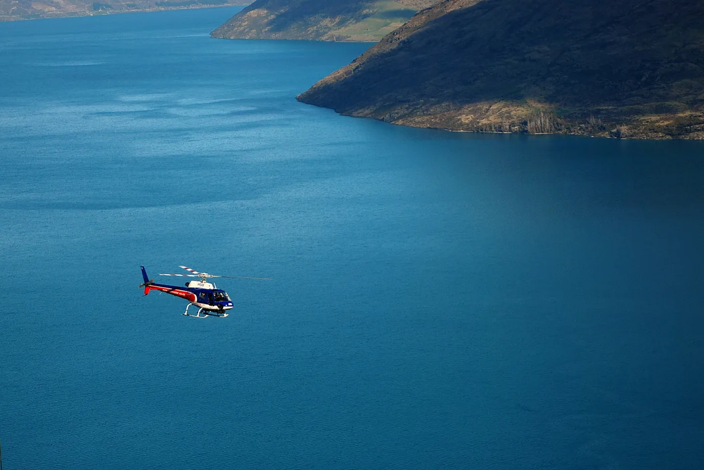 Helikopter über dem tiefblauen Wasser eines Bergsees bei Queenstown