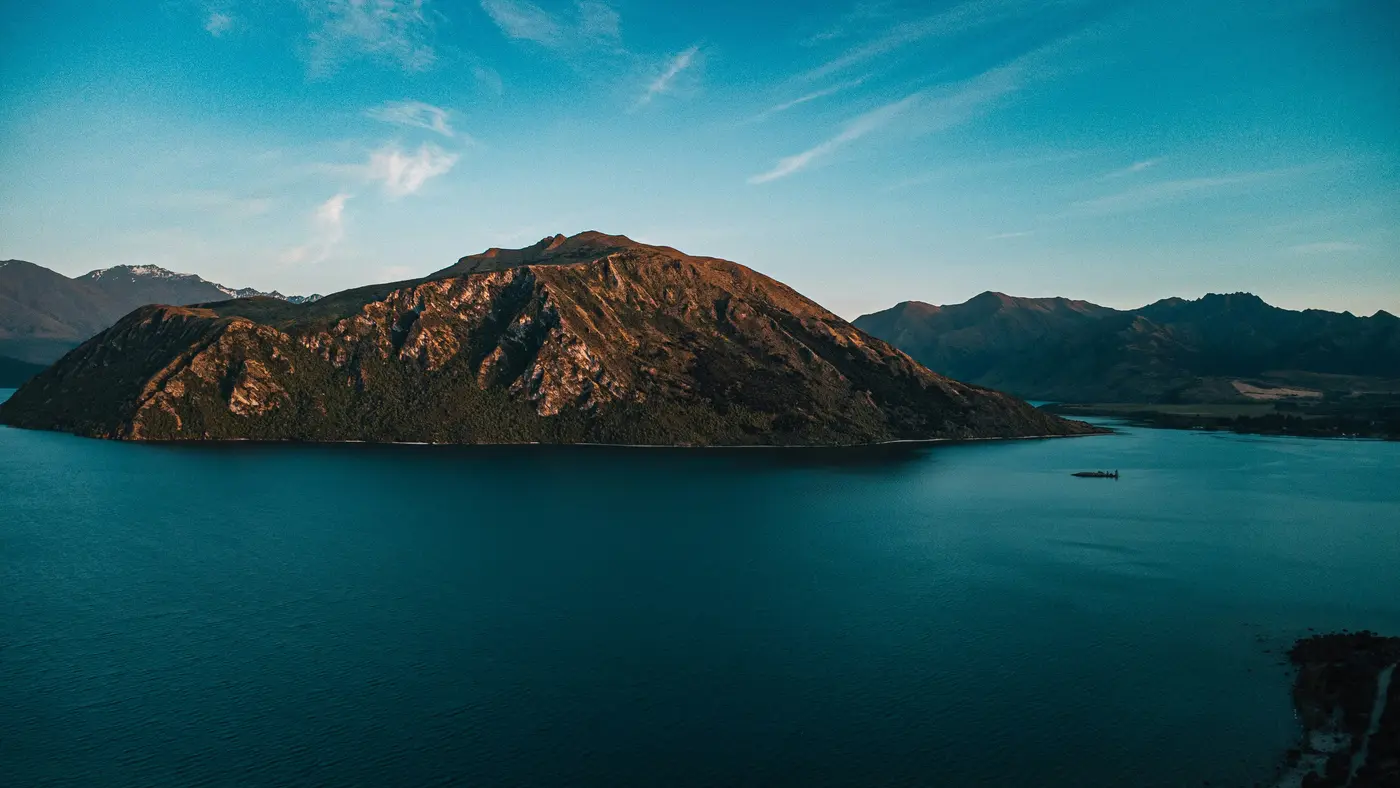 Luftaufnahme eines Bergs, der aus dem tiefblauen Wasser des Lake Wānaka aufragt